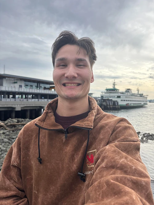 Chris Nussbaum smiling in a brown jacket, with a Puget Sound ferry behind him